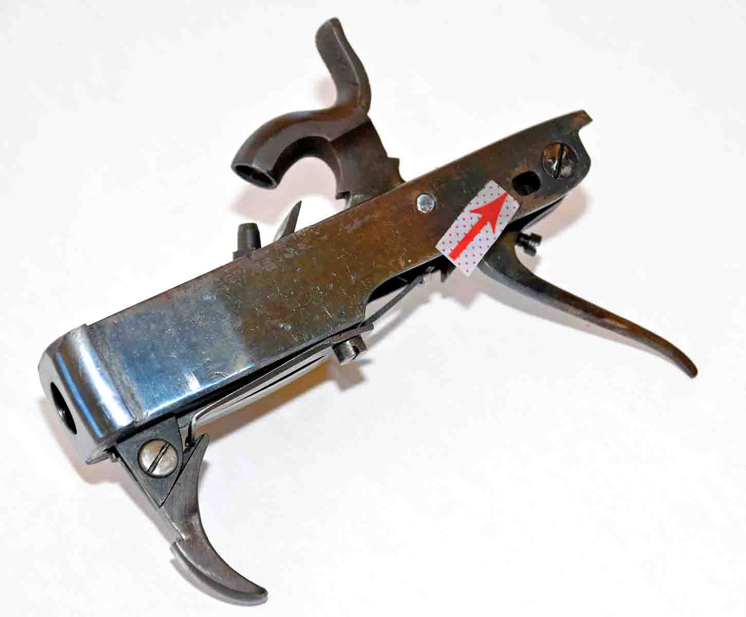 This shows the breechblock removed from the receiver. The arrow shows the pivot/tip up hole where a single screw passes through to hold the block into the receiver. Note that the hole is oval so that the block can be adjusted forward if necessary. It also allows for heat expansion from rapid firing.